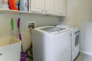 A laundry room with two white front-loading washing machines, a purple mop, and cleaning supplies on a shelf. - Lake Views & Work Spaces: Quiet Hilliard Home! (Hilliard)