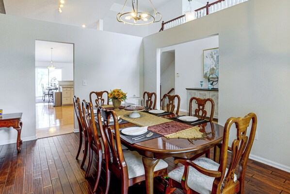 A dining room with a wooden table set for six, surrounded by chairs, and a kitchen area in the background. - Lake Views & Work Spaces: Quiet Hilliard Home! (Hilliard)