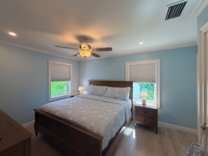 A bedroom with a bed, nightstands, a ceiling fan, and windows with blinds.