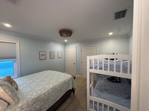 Um quarto com cama, beliche, janela com persianas e porta.