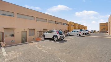 Un estacionamiento con varios autos estacionados frente a una fila de edificios con ventanas protegidas por persianas.