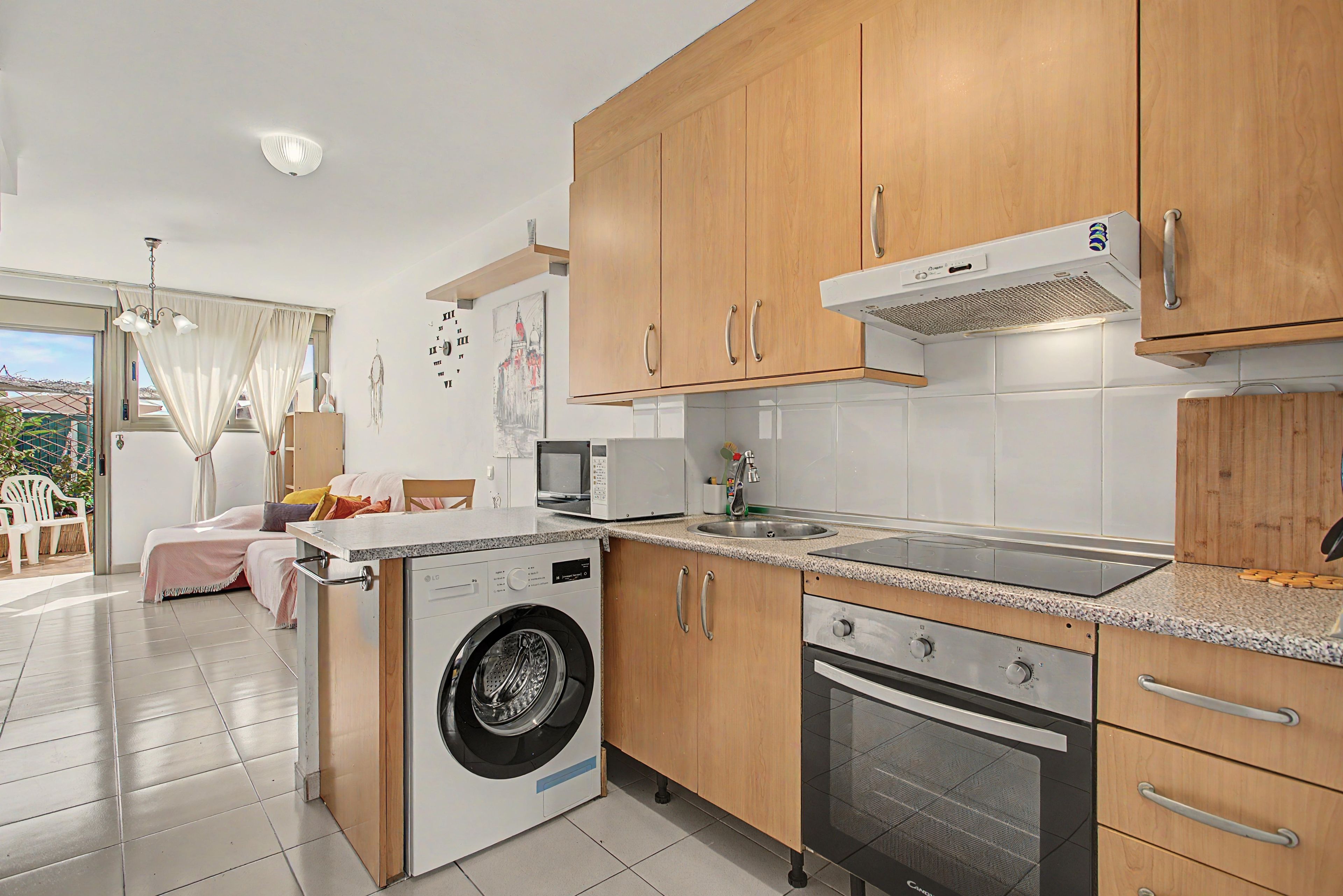 Una cocina funcional con armarios de madera, lavadora, horno y microondas.