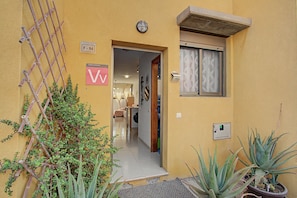 A yellow building with a bamboo fence, a door with a 'V' sign, and a window with frosted glass. - Vacation Home 'Romantic Gateway By The Sea' with Sea View, Private Terrace and Wi-Fi (Antigua)