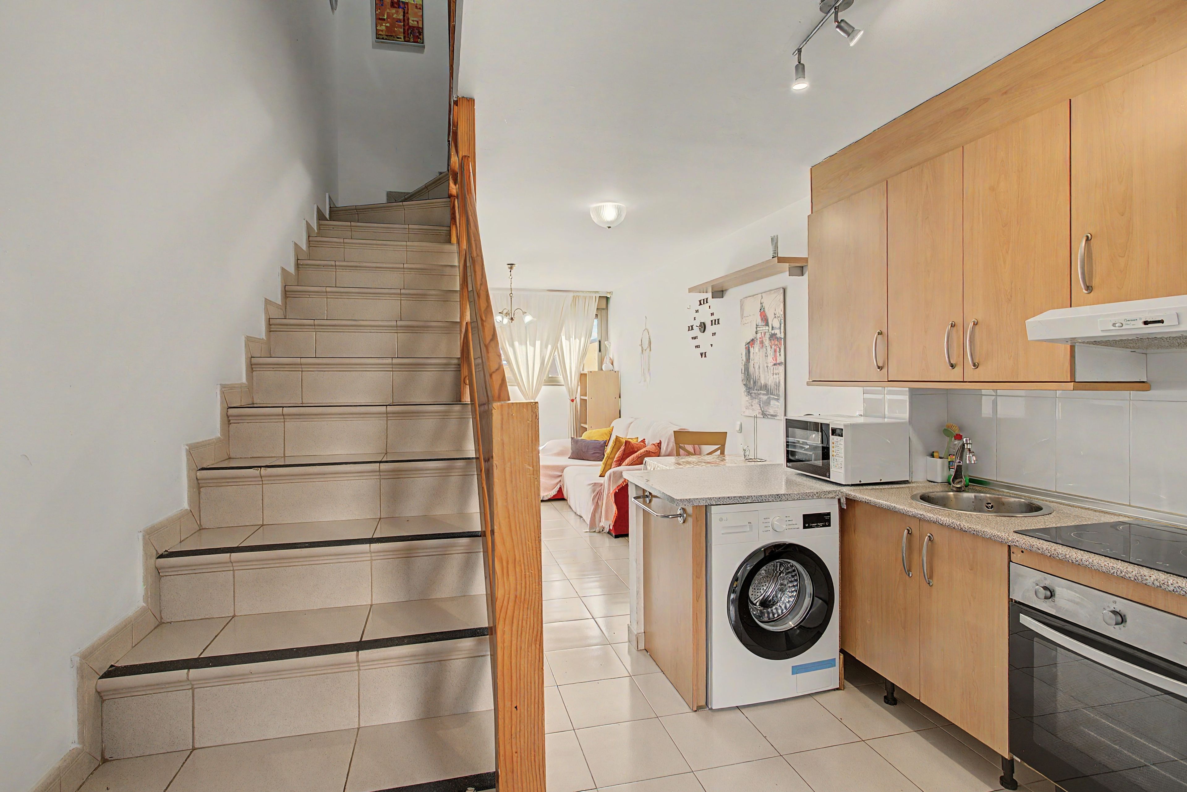 Una cocina con muebles de madera, lavadora y microondas.