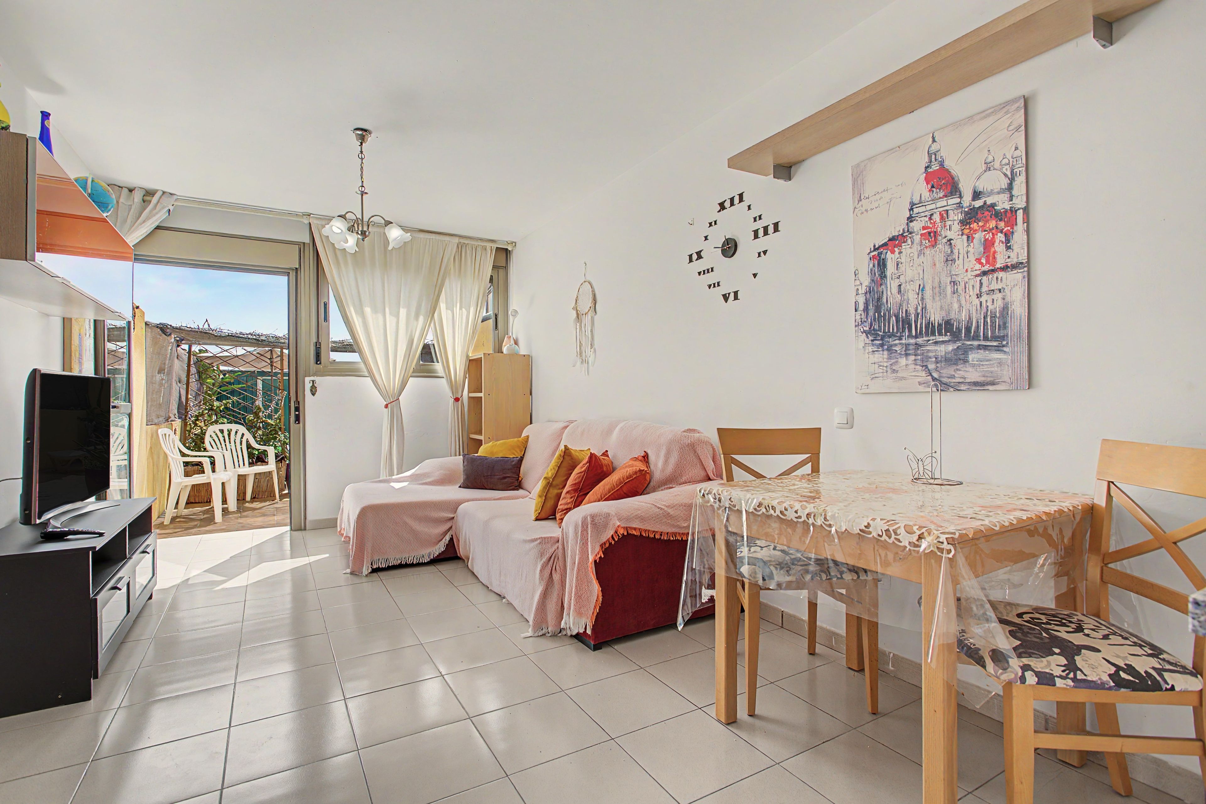 A living room with a sofa, a TV, a dining table with chairs, and a painting on the wall.