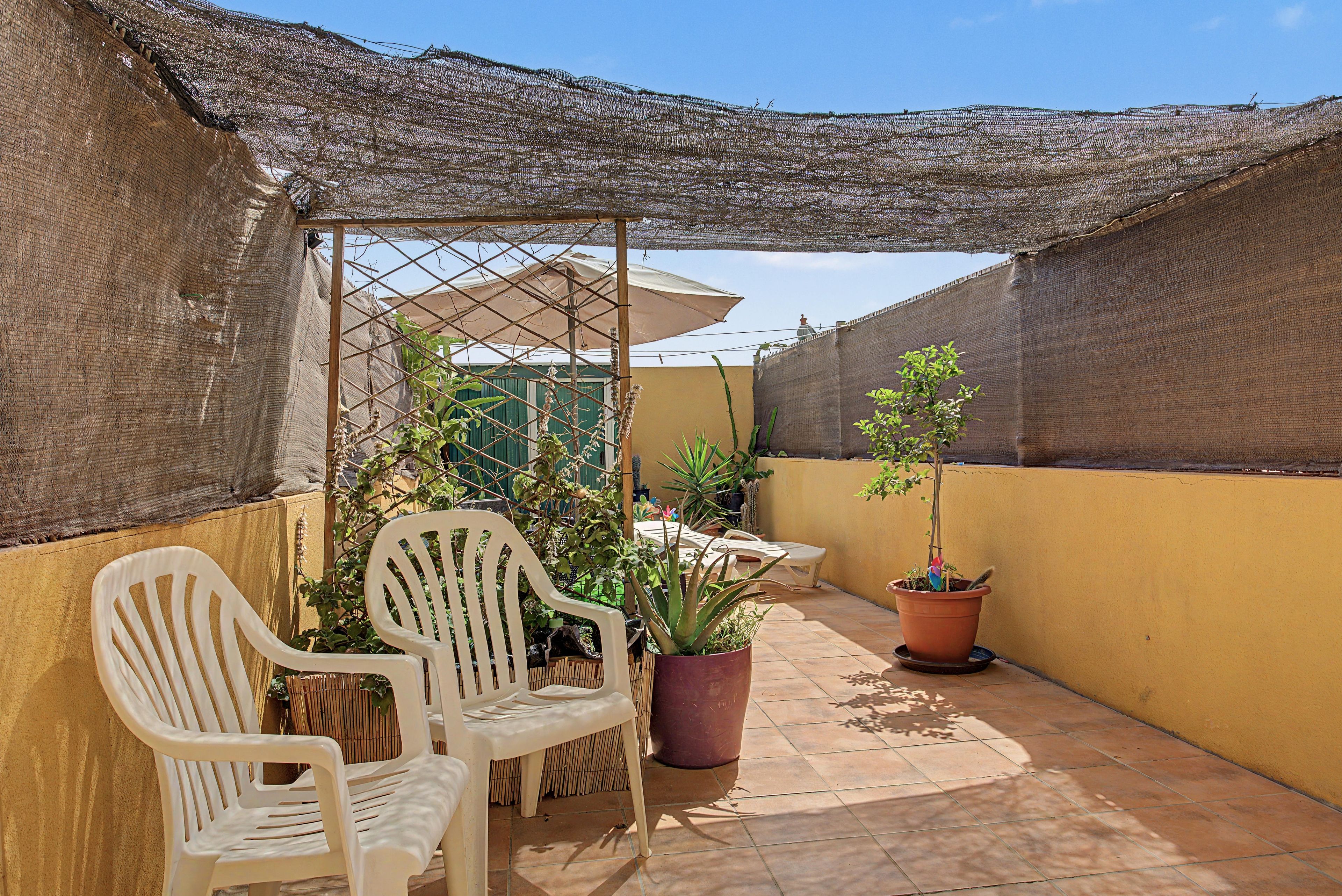 Un patio con dos sillas de plástico blanco, una mesa y plantas en macetas.