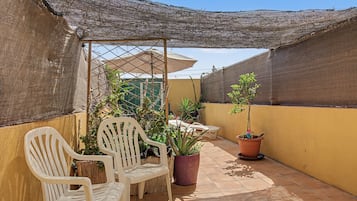Eine Terrasse mit zwei weißen Plastikstühlen, einem Tisch und Topfpflanzen.
