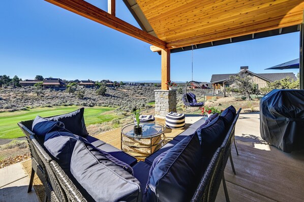A covered outdoor seating area with a view of a golf course and distant buildings.