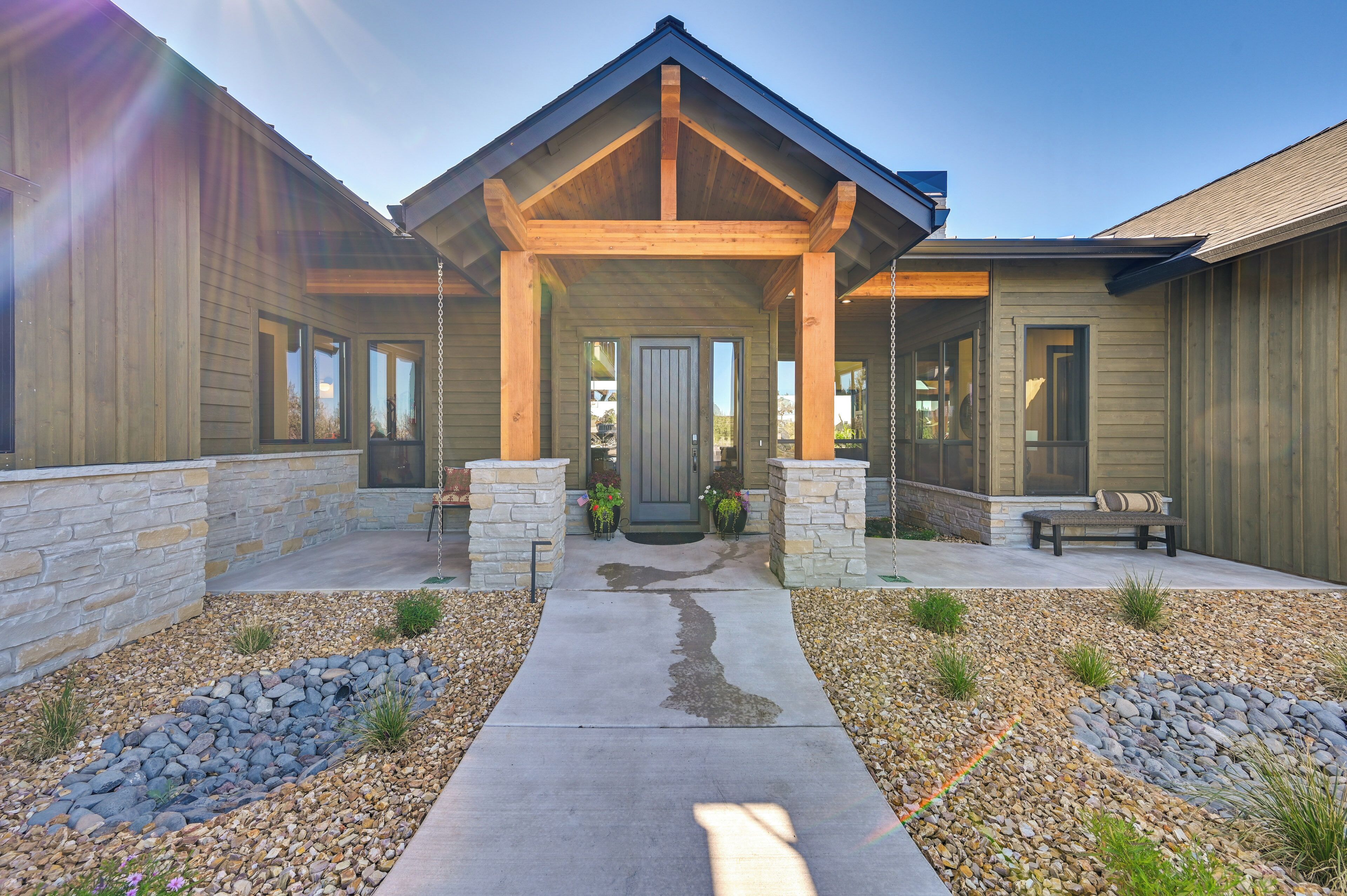 A modern house with a stone facade, a covered porch, and a concrete pathway leading to the entrance.