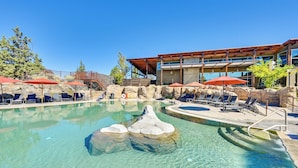 A clear pool with lounge chairs and umbrellas, surrounded by a wooden deck and a building with large windows. - Golf Views, Resort Pool Access! Brasada Ranch Home (Powell Butte)