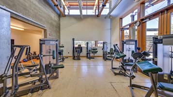 A gym with various exercise machines, a concrete wall, and large windows allowing natural light.