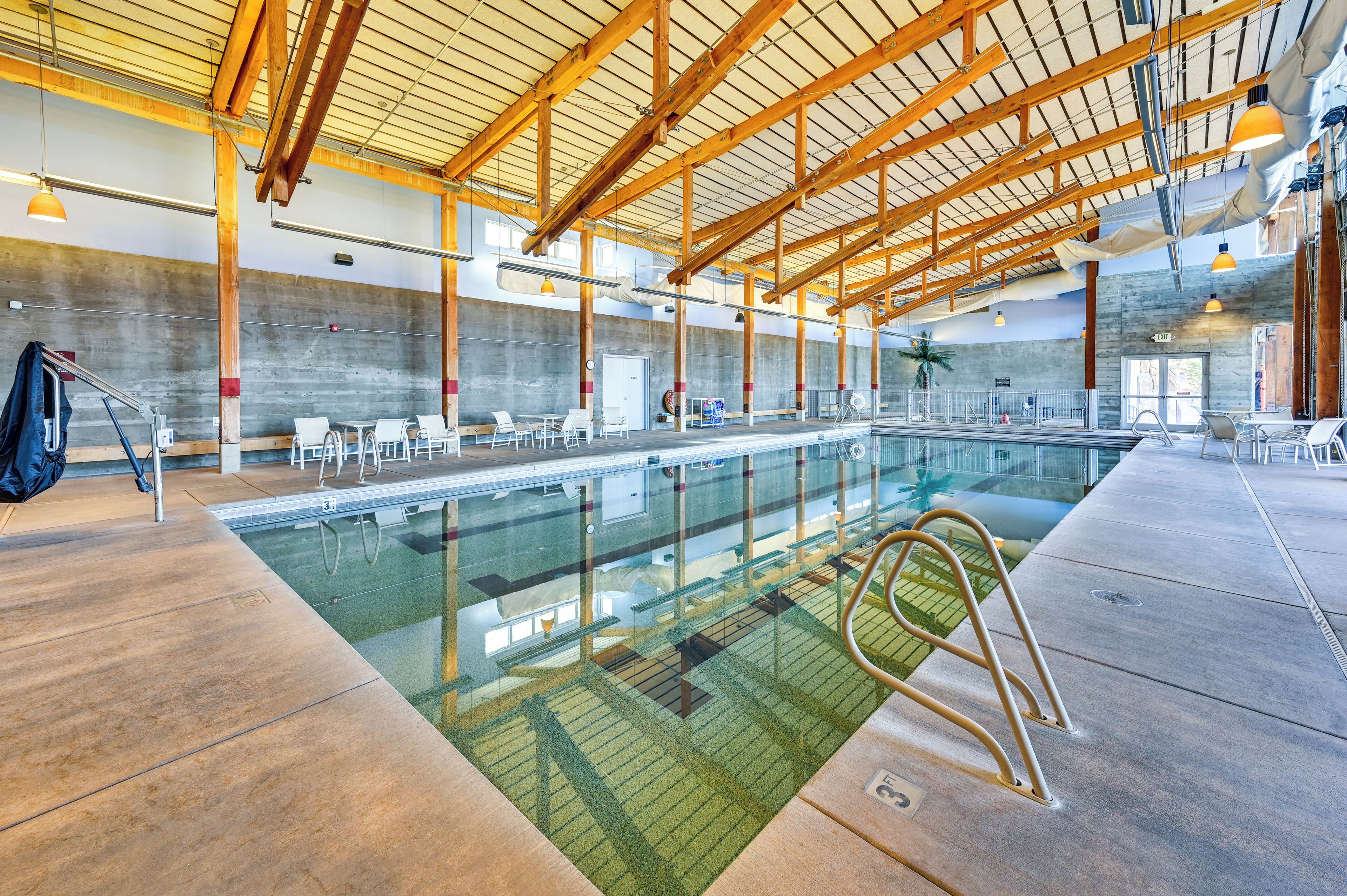 An indoor swimming pool with a high ceiling, concrete walls, and multiple seating areas.