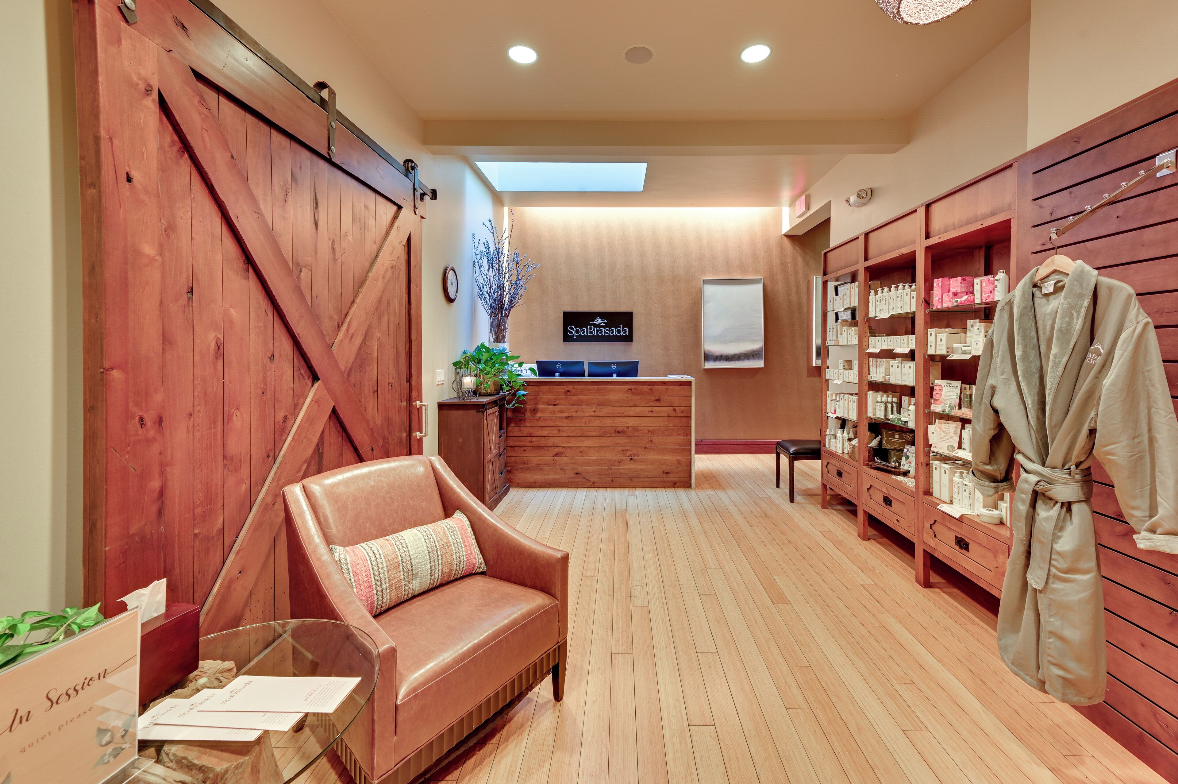 A spa room with a wooden reception desk, a massage chair, and shelves with bath products.