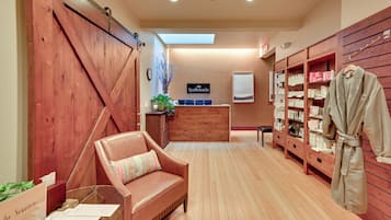 A spa room with a wooden reception desk, a massage chair, and shelves with bath products.
