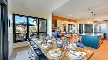 Une cuisine moderne dotée d’un grand îlot central, d’appareils électroménagers en acier inoxydable et d’un coin repas avec une longue table pouvant accueillir six personnes.