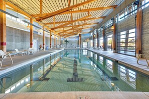 Una amplia piscina interior con techo alto y vigas de madera, rodeada de zonas de estar y grandes ventanales.