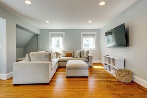 Uma sala de estar moderna com sofá seccional, pufe e TV de tela plana na parede.