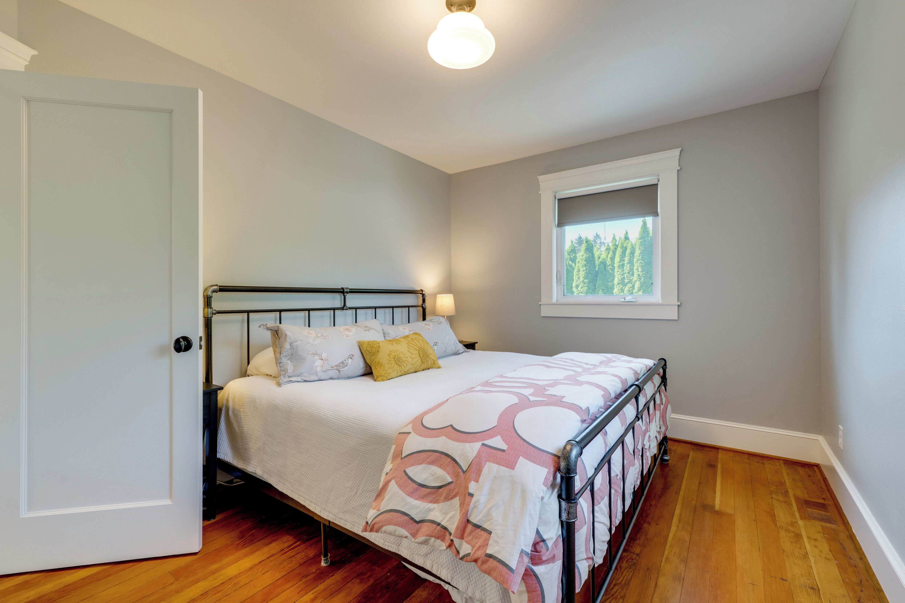 Une chambre à coucher avec un lit, une fenêtre donnant sur des arbres, une porte et un luminaire au plafond.