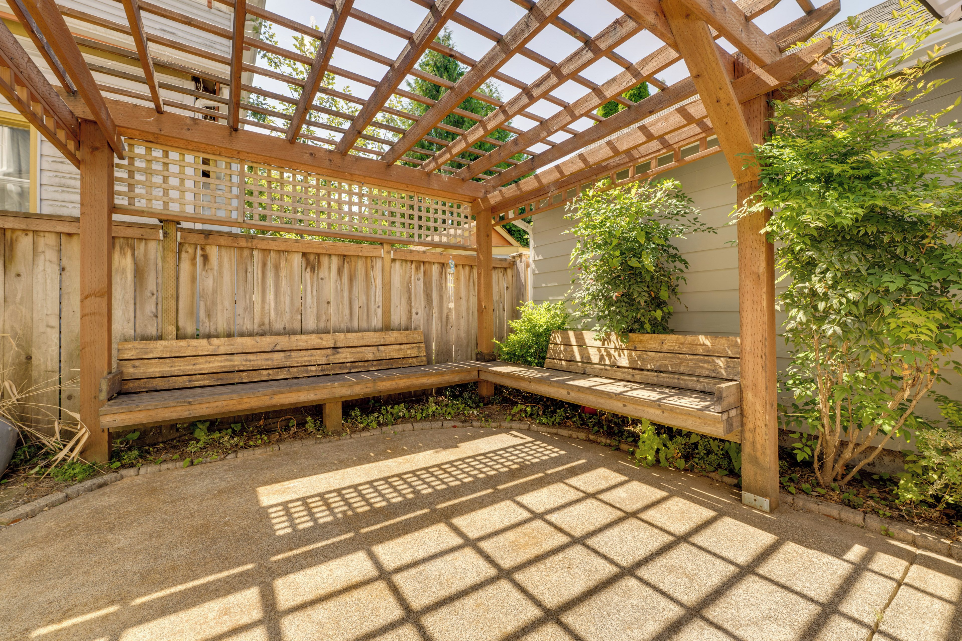 A wooden pergola with a bench, surrounded by a wooden fence and greenery.