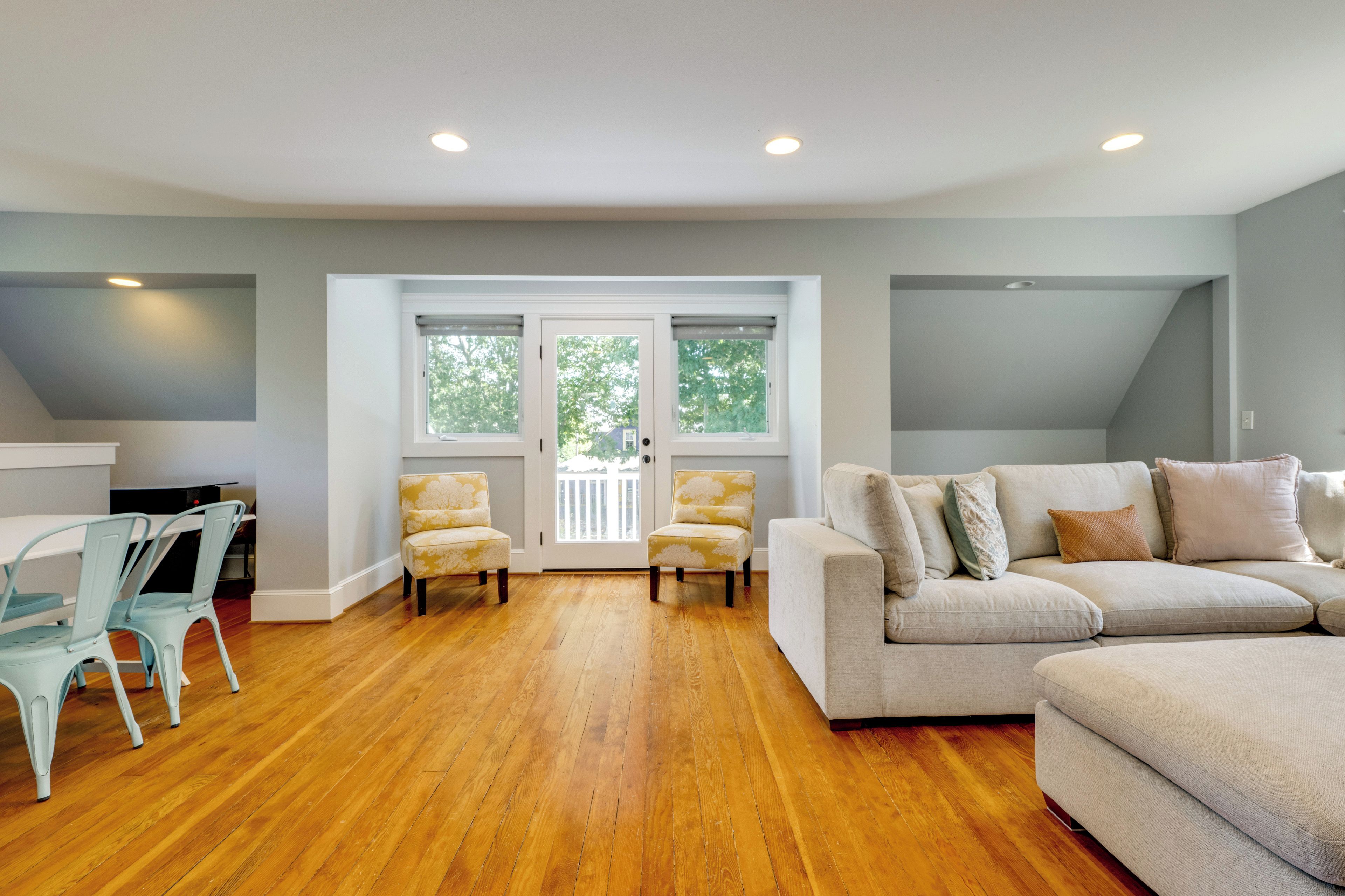 A spacious living room with hardwood flooring, a white sofa set, and two armchairs.