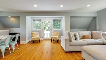 A spacious living room with hardwood flooring, a white sofa set, and two armchairs.