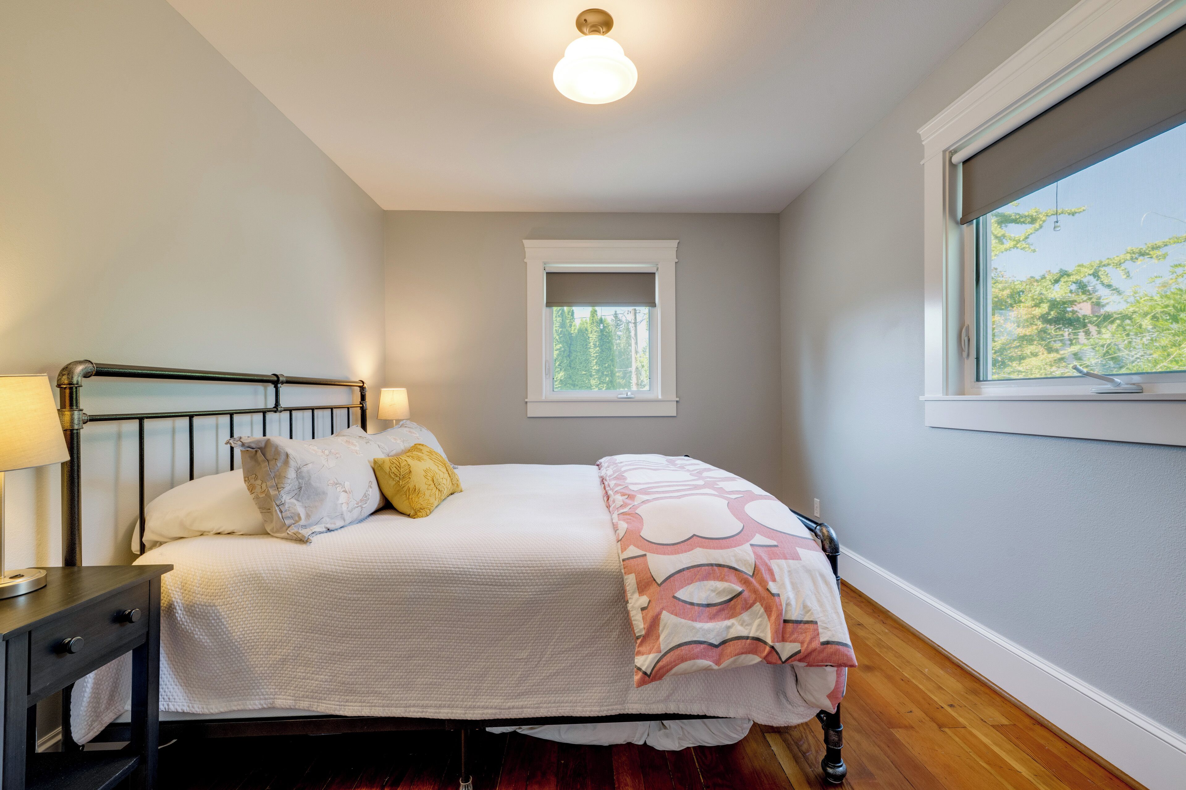 A bedroom with a bed, nightstand, lamp, window, and a view of trees.