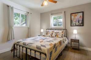 A bedroom with a bed, two bedside lamps, a ceiling fan, and a painting on the wall.