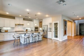 Uma cozinha moderna com armários brancos, uma ilha central com banquetas, eletrodomésticos de aço inoxidável e piso de madeira.