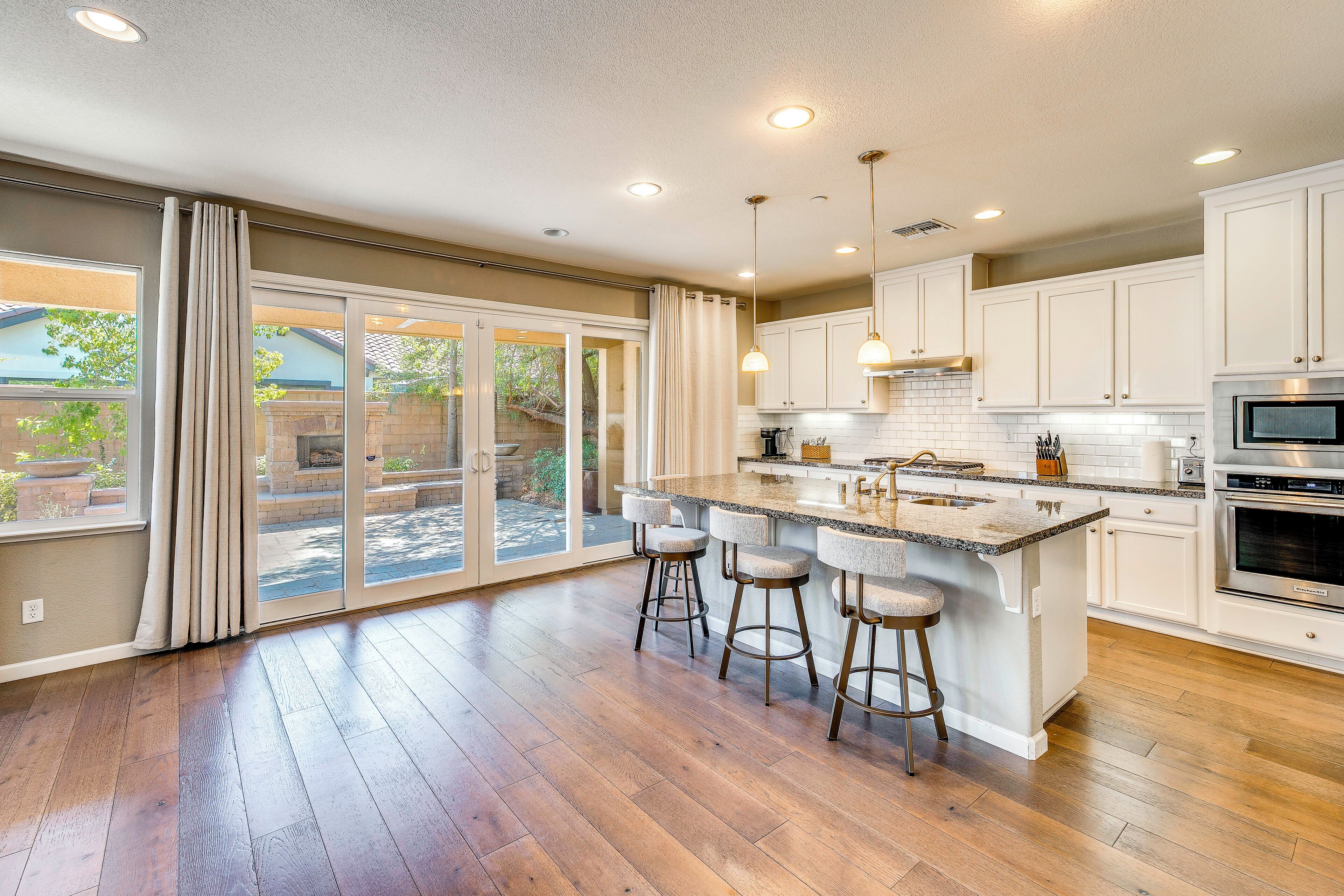 A modern kitchen with a large island, bar stools, and a sliding glass door leading to a patio.