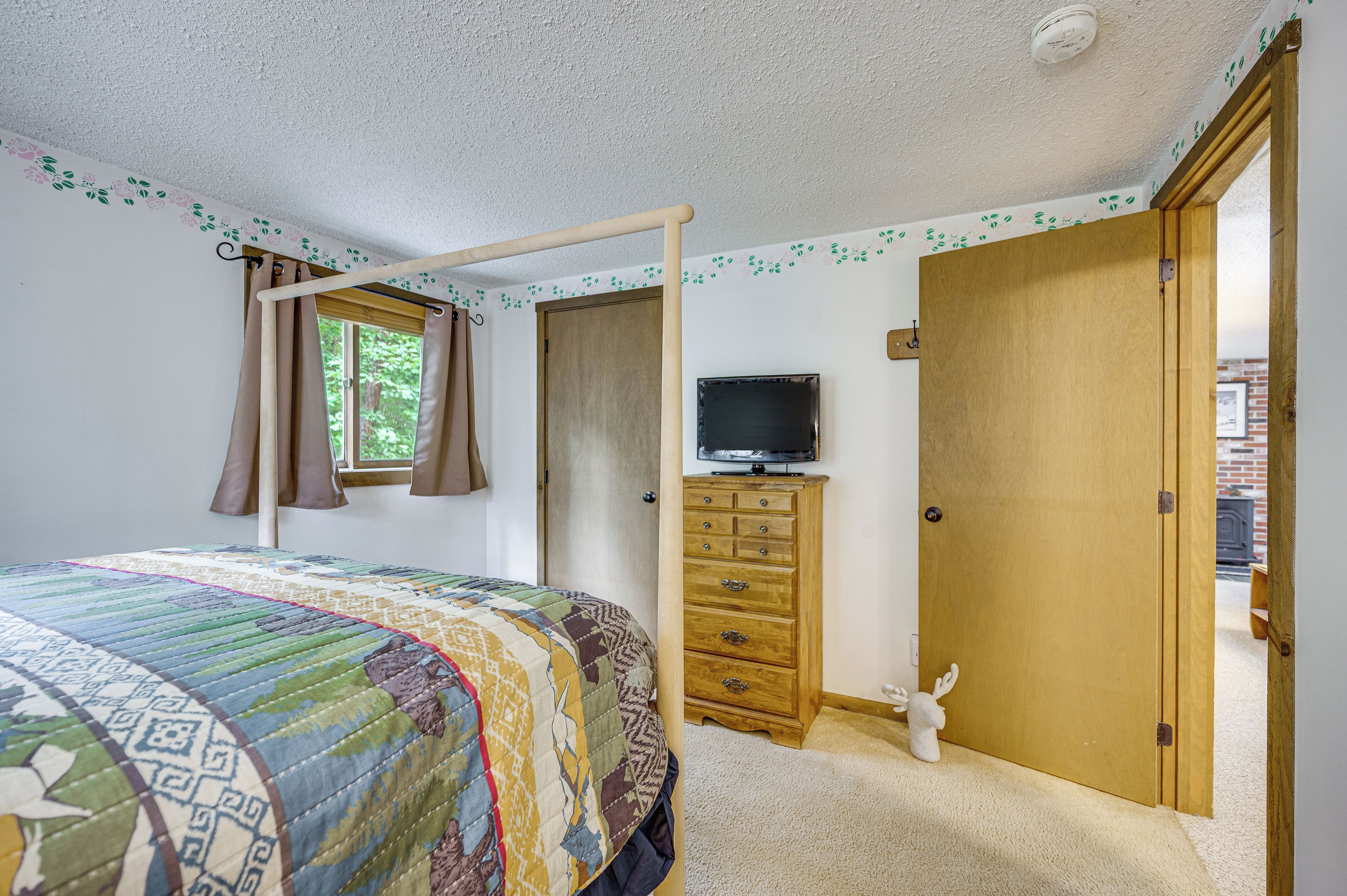 Une chambre à coucher comprenant un lit, une commode, un téléviseur et une porte donnant sur une autre pièce.
