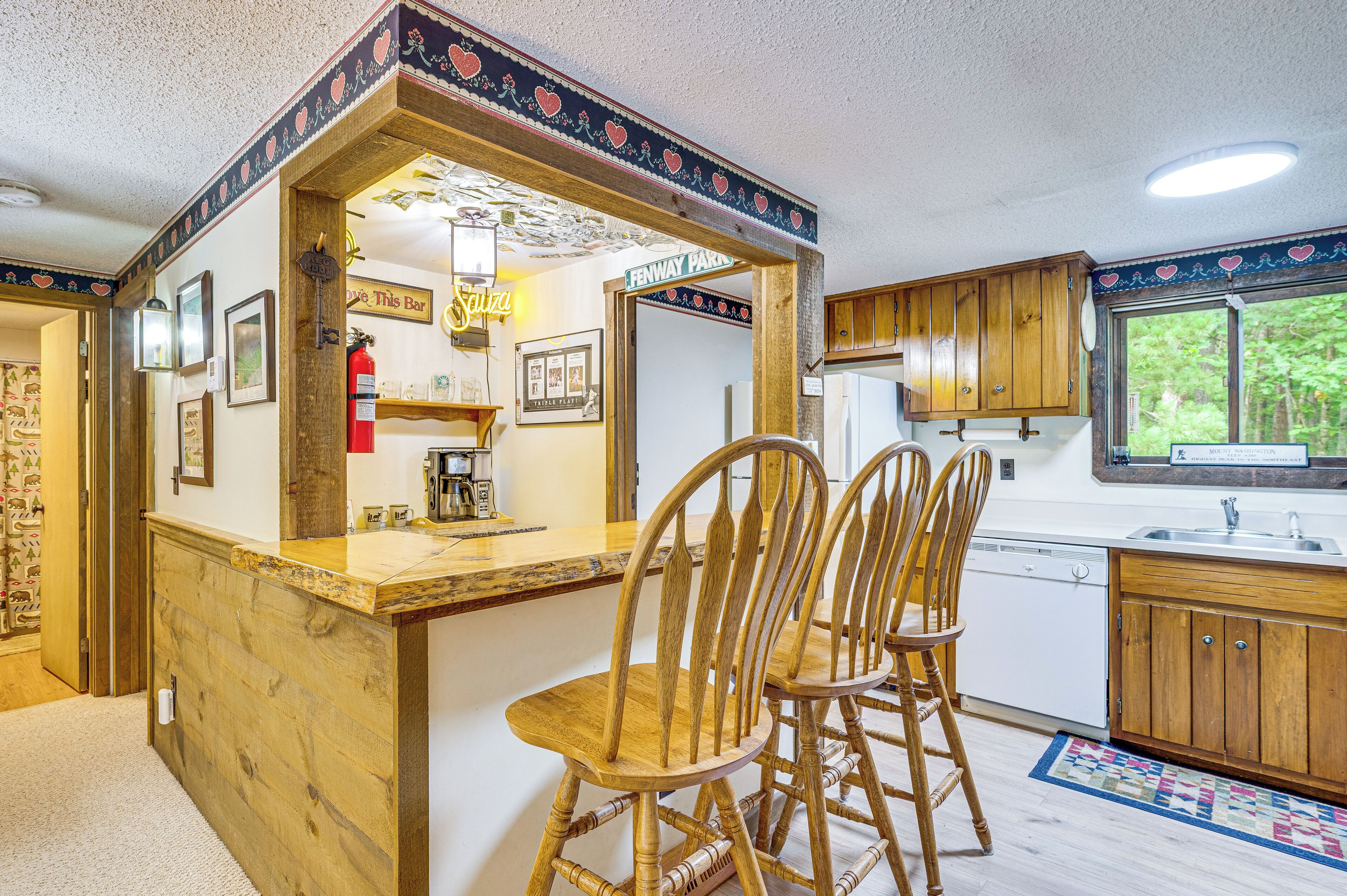 A kitchen with wooden cabinets, a bar area with a neon sign, and a window with a view of trees.