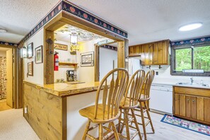 A kitchen with wooden cabinets, a bar area with a neon sign, and a window with a view of trees.