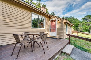 Eine Holzterrasse mit Gartenmöbeln, einer Tür und einem Fenster mit Blick auf einen Wald.