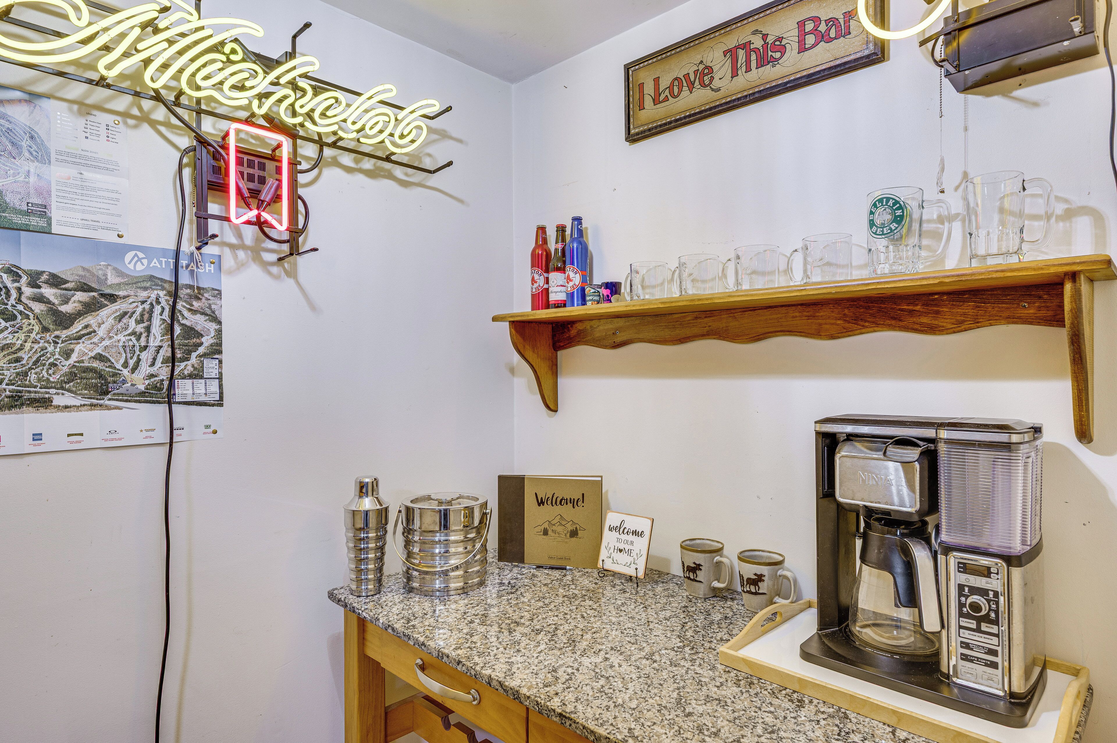 A bar area with a neon sign, shelves with bottles, glasses, and a coffee machine.