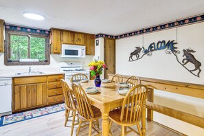 Une cuisine avec des meubles en bois, un four à micro-ondes et une cuisinière. On y trouve une table à manger avec des chaises et un vase de fleurs. Un panneau d’accueil orné de silhouettes d’animaux est accroché au mur.