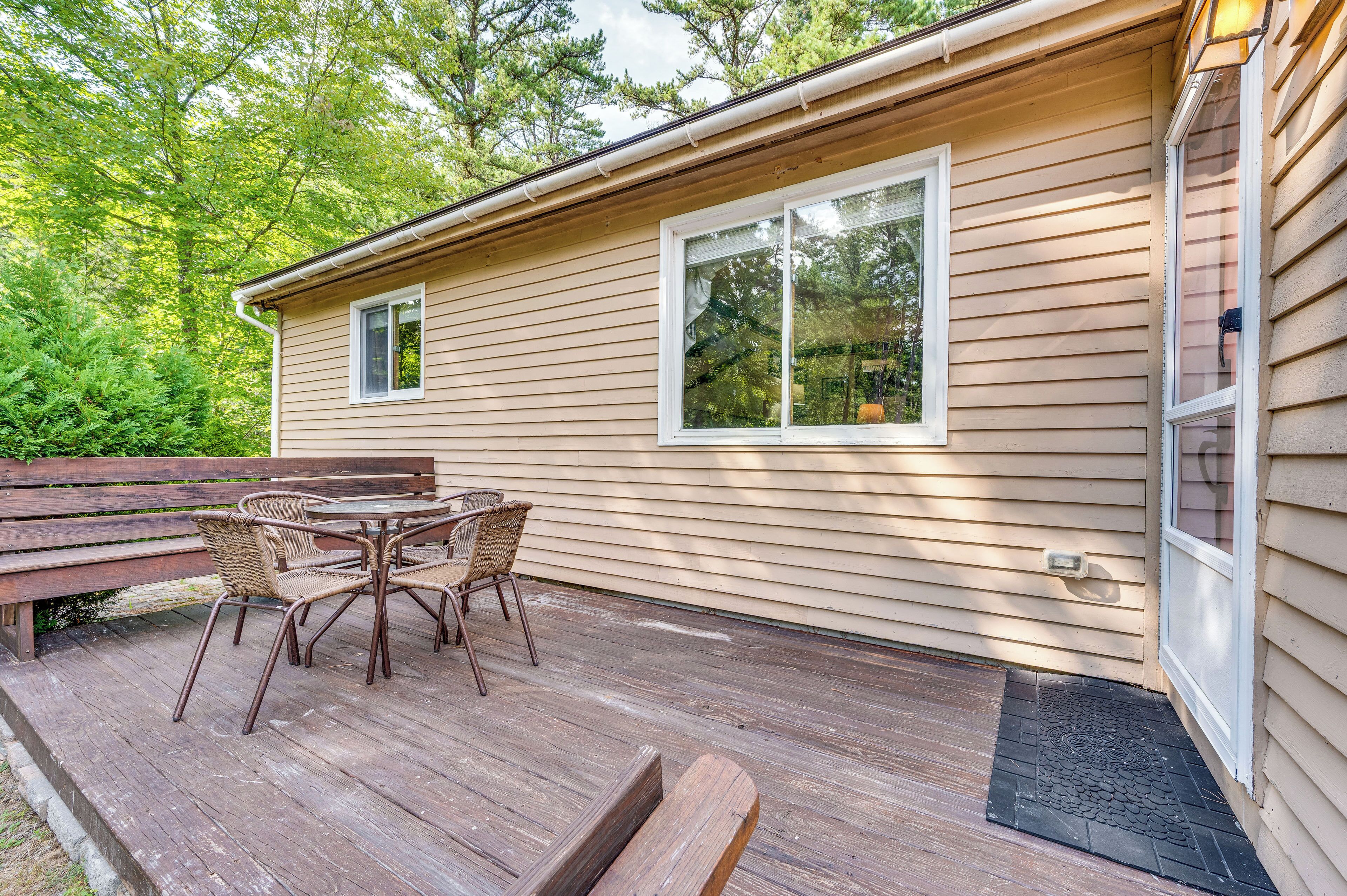 A wooden deck with a table and chairs, a bench, and a house with two windows.
