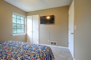 Un dormitorio con cama, ventana, televisor montado en la pared y puerta.