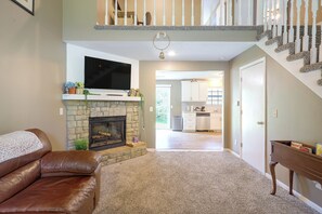 Una sala de estar con chimenea, un sofá de cuero marrón, un televisor montado sobre la chimenea y una escalera que conduce a un nivel superior.