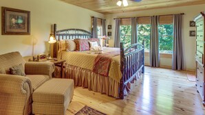 Un dormitorio con techo de madera, una cama con cabecera, una silla, un aparador y una ventana con cortinas.