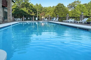 Una piscina rectangular con un muro de piedra en un lado y una terraza de madera con sillones de descanso en el otro.