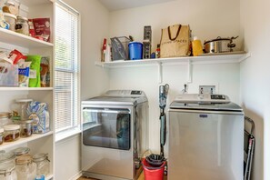 Un cuarto de lavandería con dos lavadoras, un estante con productos de limpieza y una ventana con persianas.