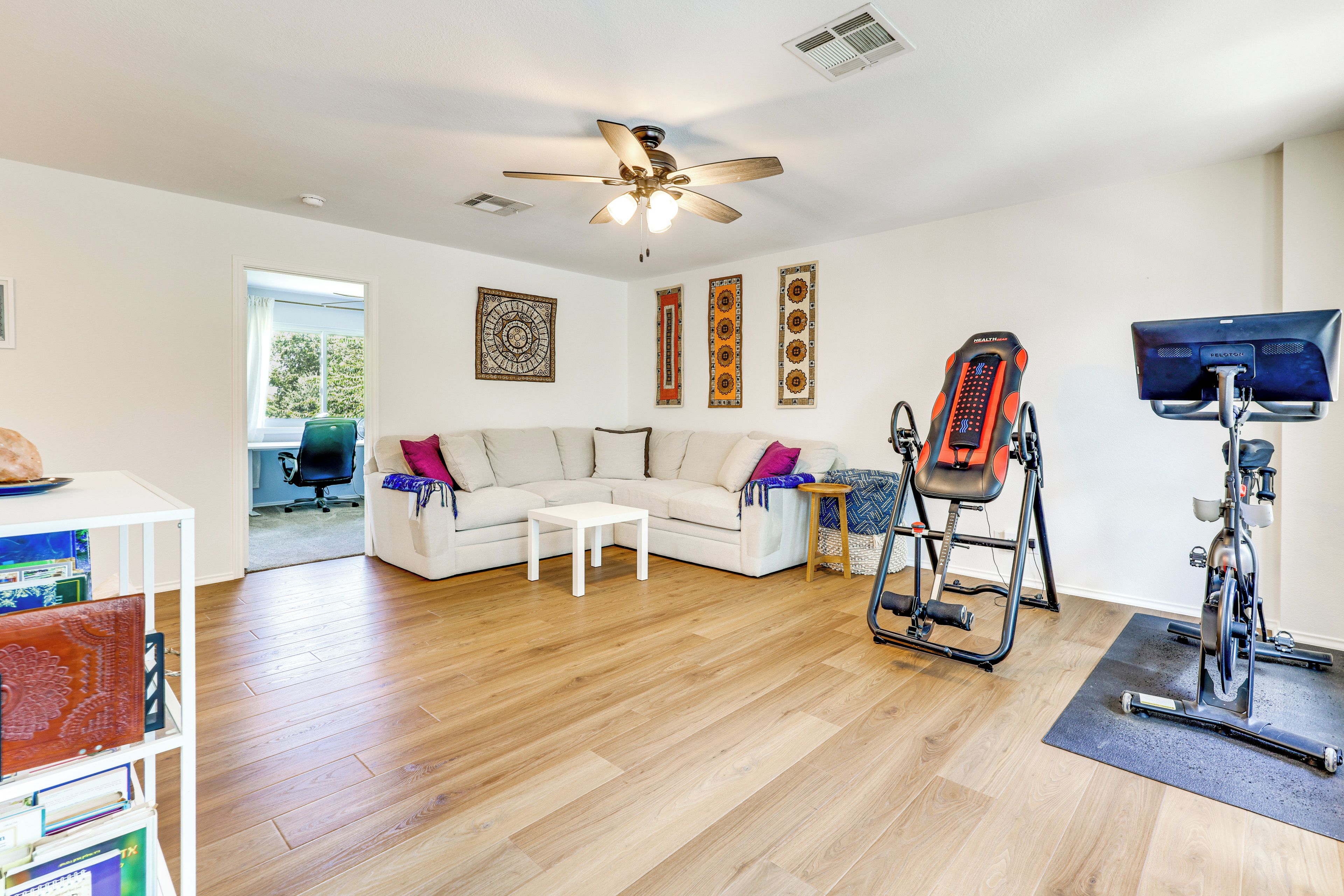 A spacious living room with a white sofa, a ceiling fan, and exercise equipment.