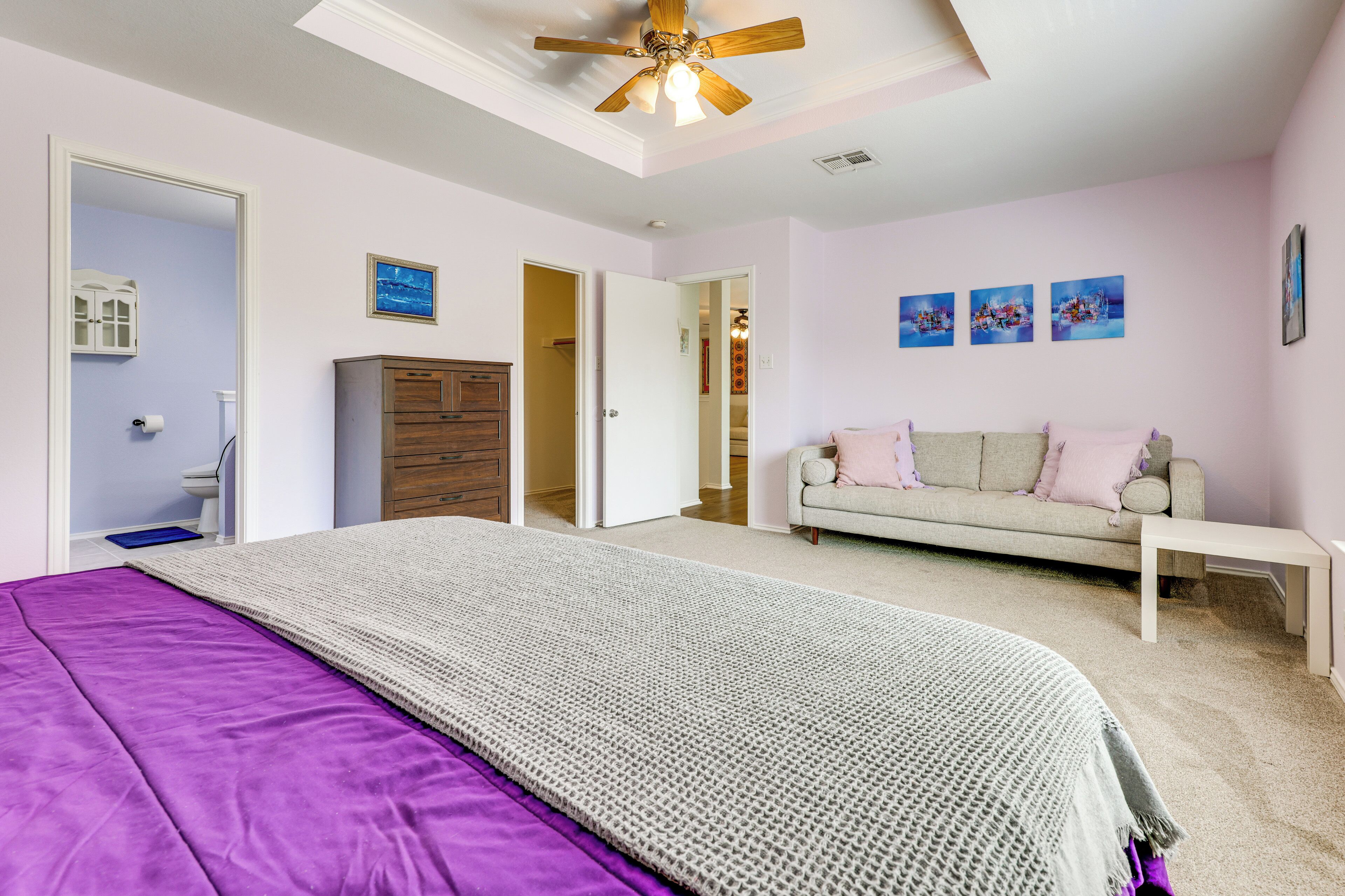 A bedroom with a bed, a dresser, a sofa, and a ceiling fan.