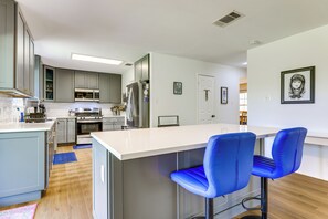 Una cocina moderna con electrodomésticos de acero inoxidable, una zona de bar con sillas azules y una encimera blanca.