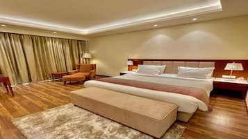 A hotel room with a large bed, a sitting area with a chair, a small table, and a bench.