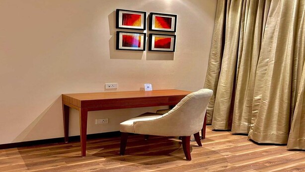 A room with a wooden desk, a white chair, and a wall-mounted artwork. - Superior Checkin Amritsar (Amritsar)