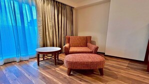 A room with a wooden floor, a brown armchair, a small round table, and a window with sheer curtains. - Superior Checkin Amritsar (Amritsar)