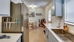 A kitchen with a refrigerator, knives, a coffee machine, and a dining area with chairs and a table. - Remote Work Ready! Walkable Fayetteville Home (Fayetteville)