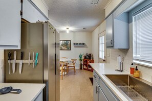 Una cocina con refrigerador, cuchillos, cafetera y comedor con sillas y mesa.