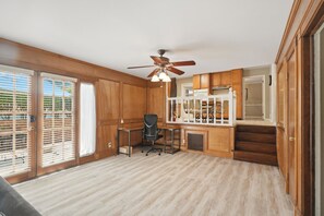 A room with wooden paneling, a ceiling fan, a desk with a chair, and a view through large windows. - Private Pool, Patio! Spacious Home in Decatur (Decatur)